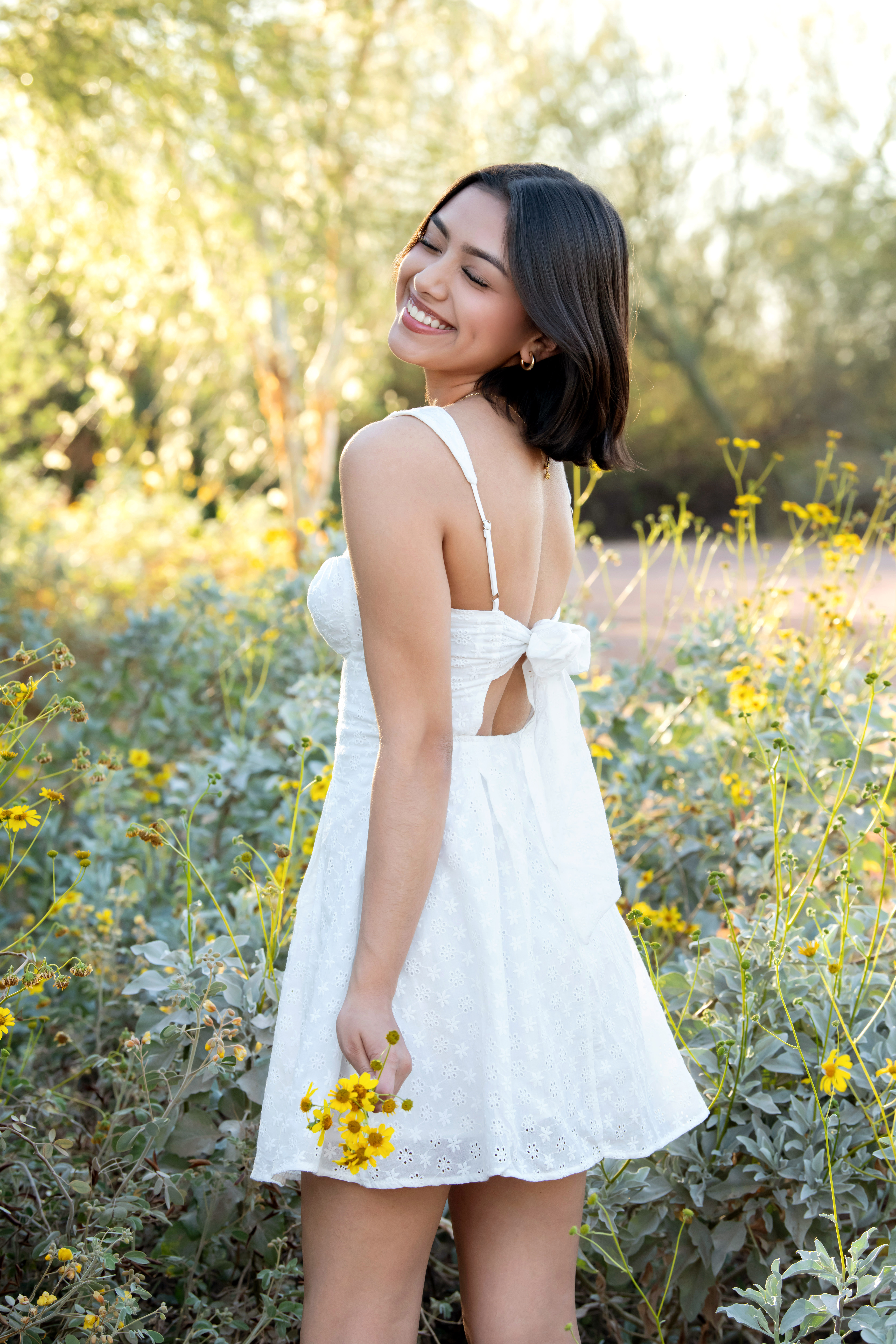 High school senior in a white dress holding yellow flowers at West Wetlands Park in Yuma, Arizona.